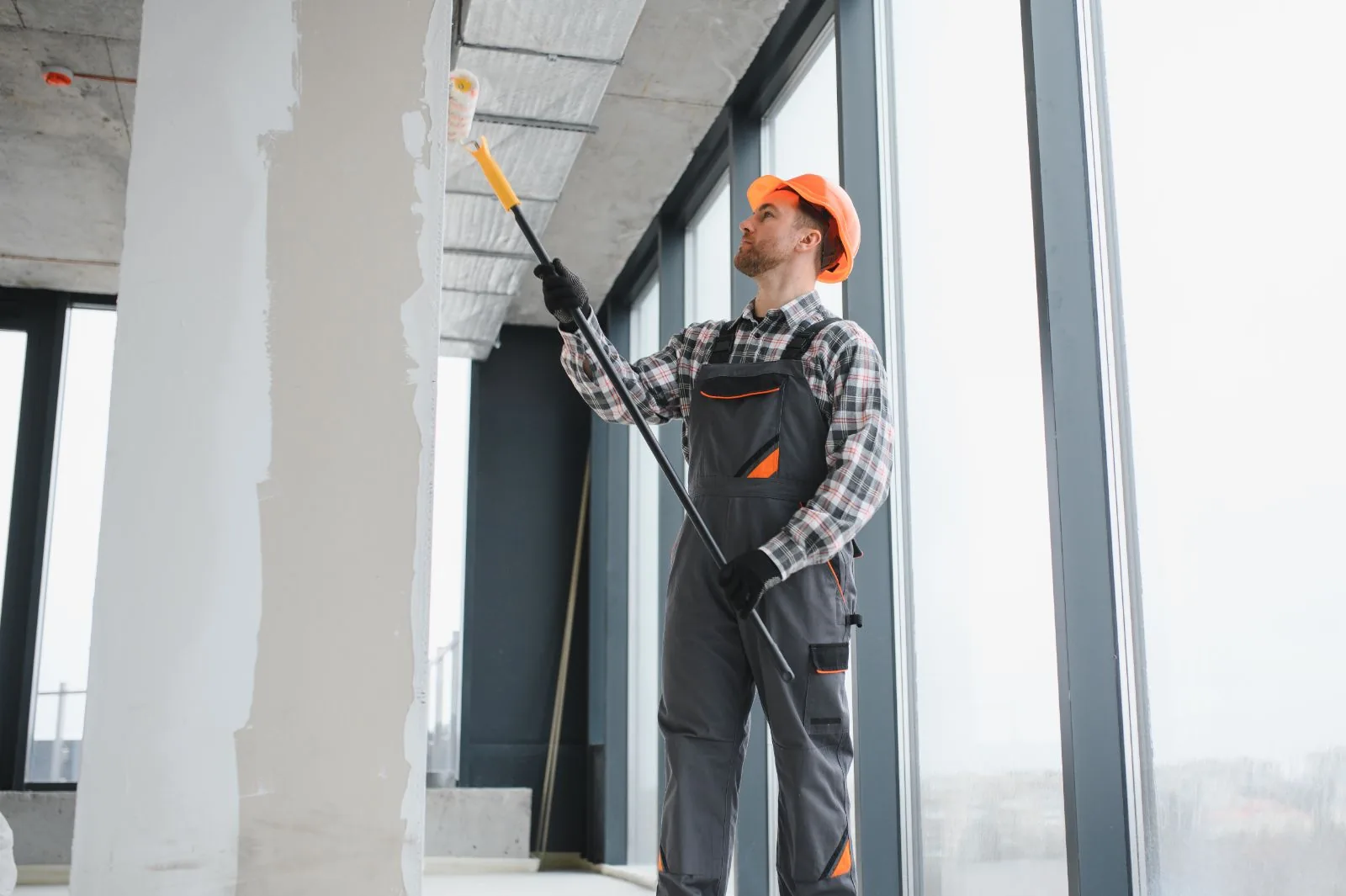 Commercial painter in a hard hat rolling paint onto an office wall with an extension pole, West Palm Beach, FL