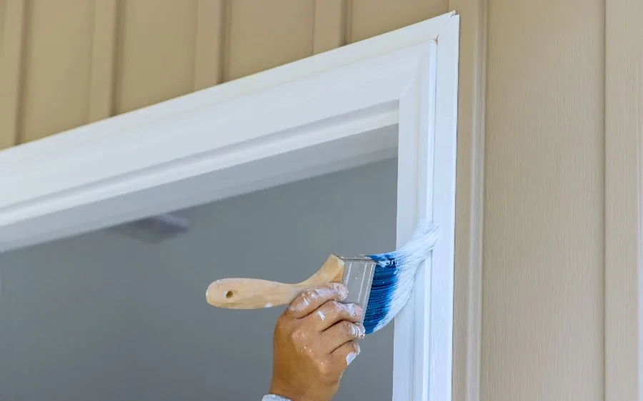 Painter cutting in a white door frame by hand against tan board-and-batten siding, Delray Beach, FL