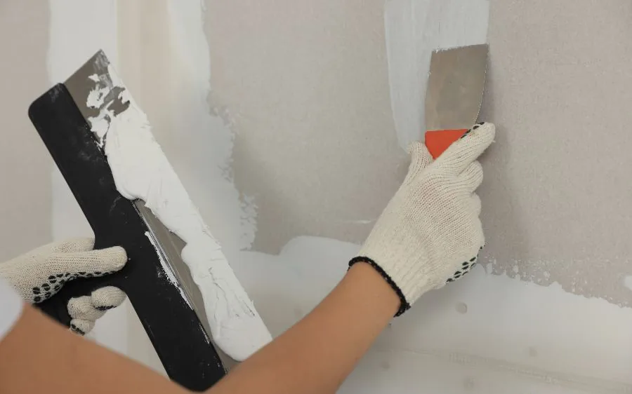 Gloved hands applying joint compound over taped drywall seams with a putty knife, West Palm Beach, FL