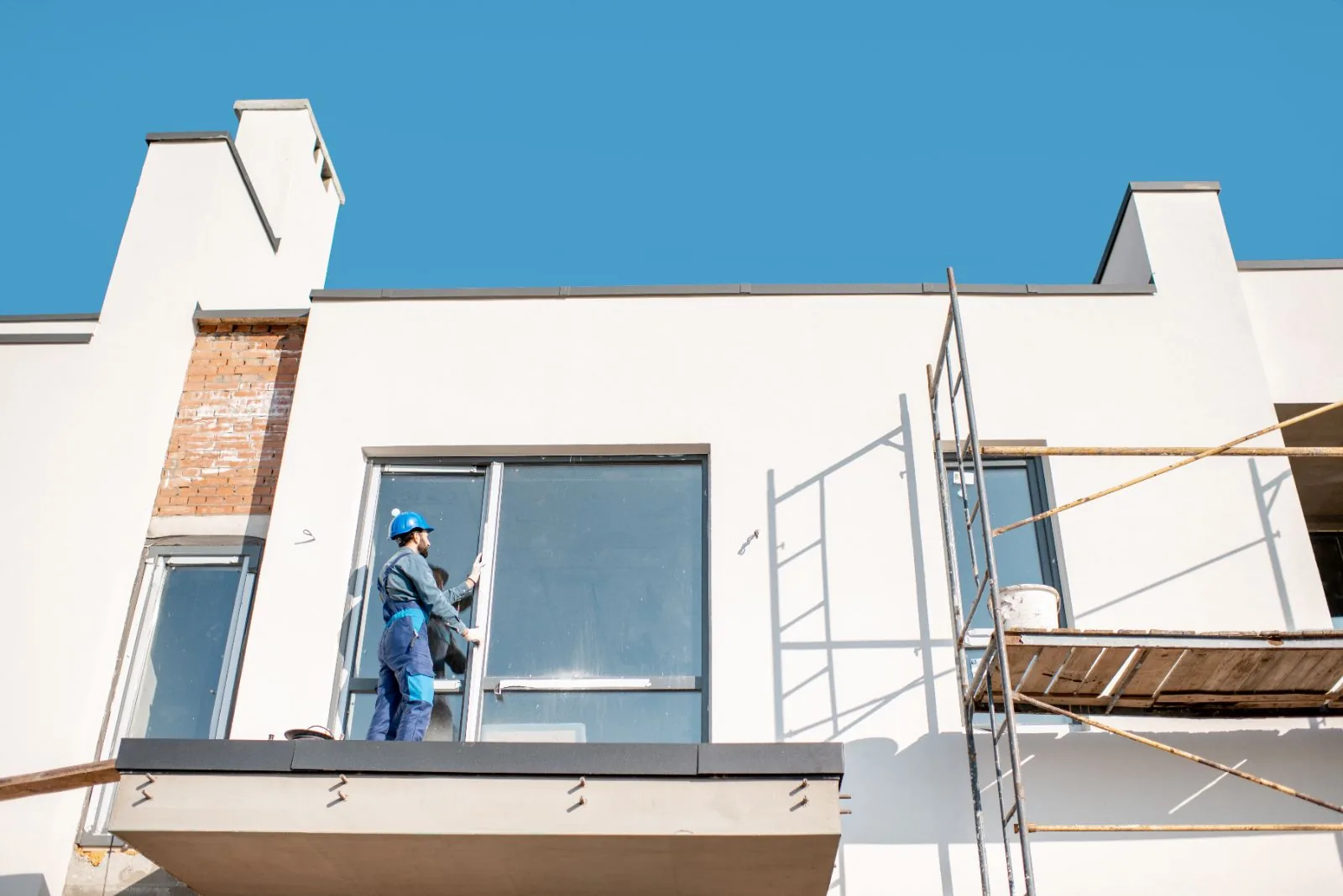 Exterior prep on a white stucco home with scaffolding and a worker at the window, Fort Lauderdale, FL