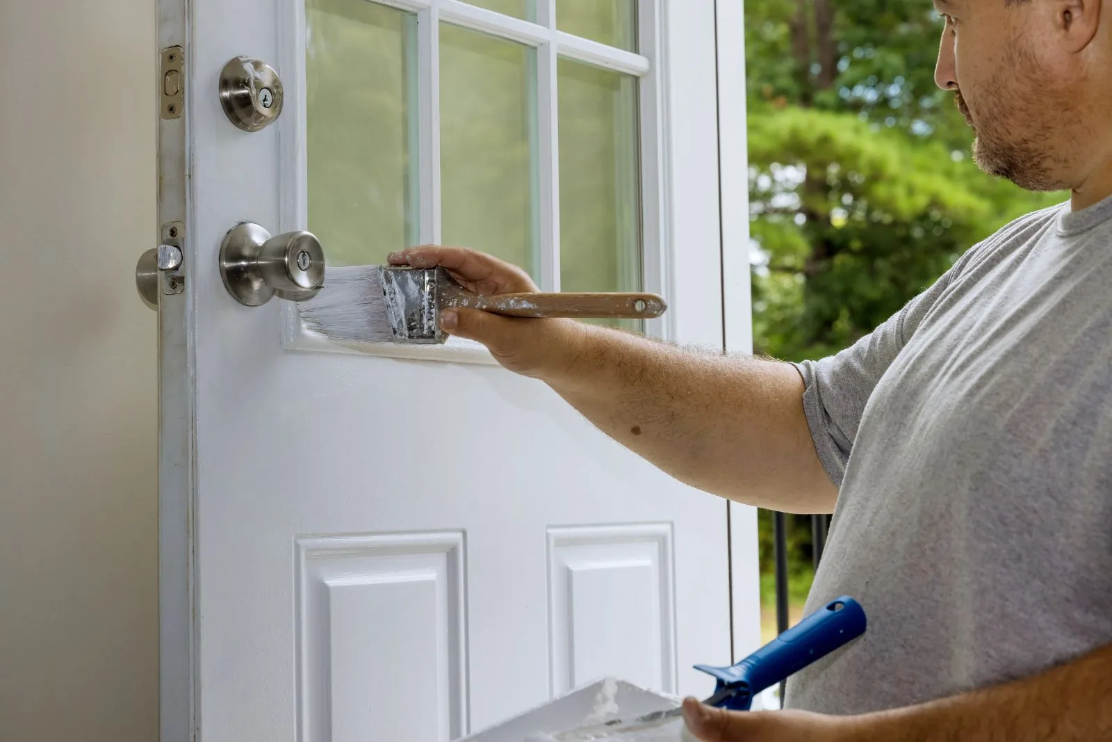 Painter brushing fresh white paint onto a front door panel beside brushed nickel hardware, West Palm Beach, FL