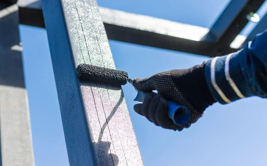 Close-up of a painter rolling navy blue paint onto an exterior metal frame, Lake Worth Beach, FL