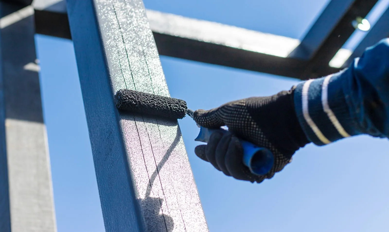 Close-up of a painter rolling navy blue paint onto an exterior metal frame, Lake Worth Beach, FL
