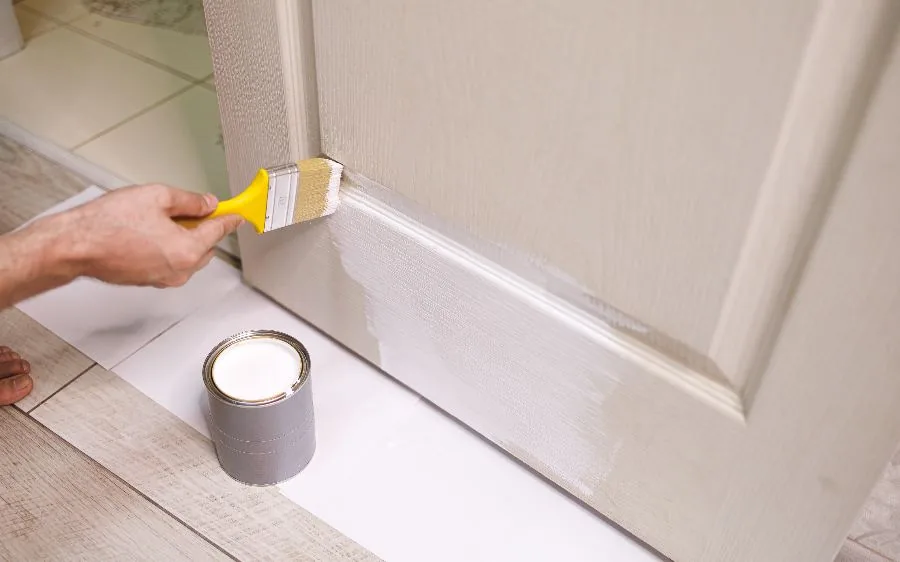 Brushing white paint onto door casing and baseboard trim with the floor masked, Boca Raton, FL