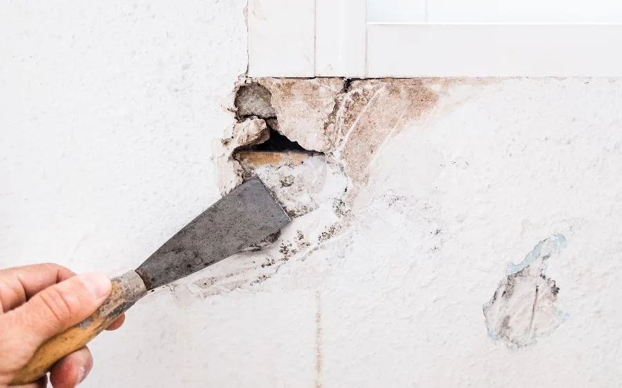 Scraping loose material from a damaged drywall hole below a window before patching, Boca Raton, FL
