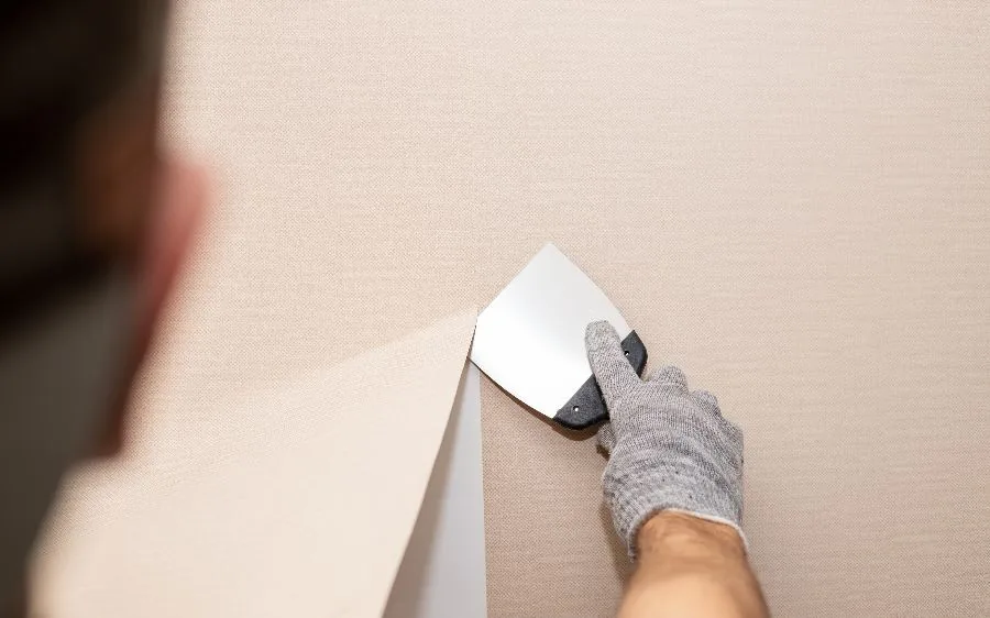 Gloved hand peeling back a strip of textured wallpaper with a putty knife to reveal the clean wall underneath, Boca Raton, FL