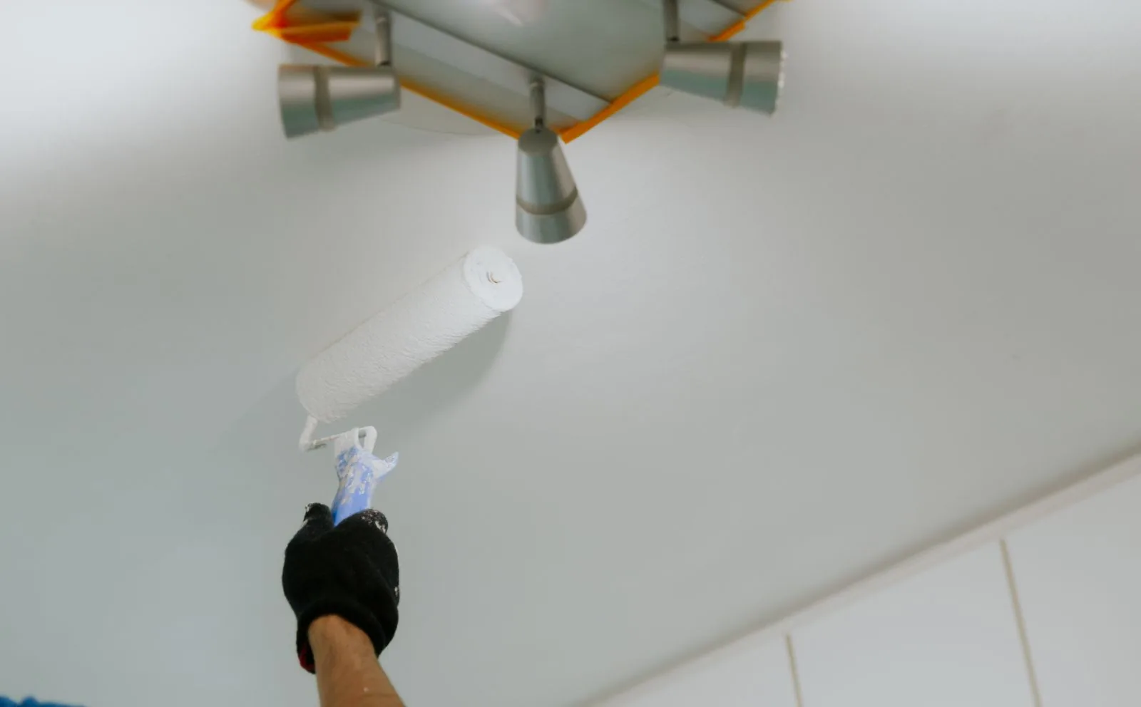Painter rolling fresh white paint onto a smooth ceiling around a masked light fixture, West Palm Beach, FL