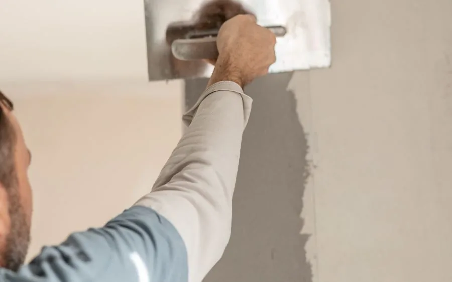 Painter skim coating a stucco wall with a steel trowel to smooth cracks before paint, Delray Beach, FL