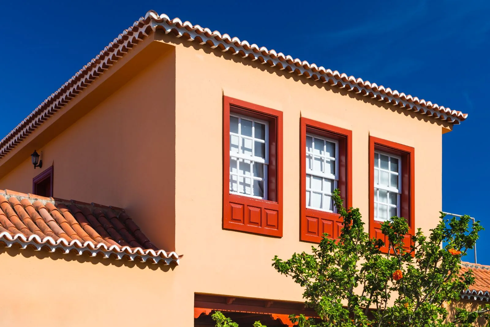 Spanish-style home exterior painting in warm terracotta with red painted window trim and barrel tile roof, Boca Raton, FL