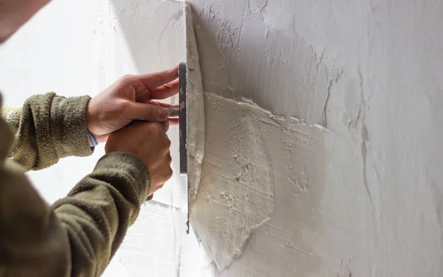 Close-up of a trowel pressing patch compound into a cracked stucco wall before repainting, Boca Raton, FL